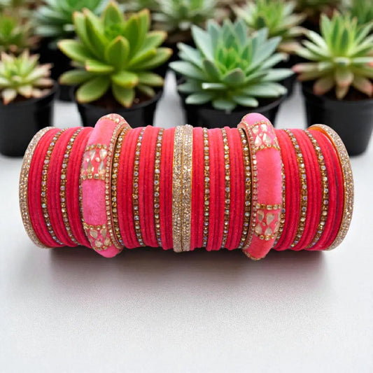 Stack of pink and gold bangles on a white surface with succulents in the background